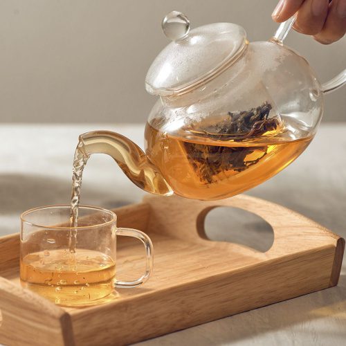 Hot water being poured over dried Moringa leaves in a glass cup
